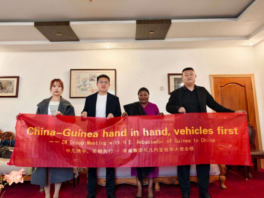 Chairman Ivan Sun and ZW Group delegation with Guinean Ambassador Aminata Koita holding a cooperation banner.